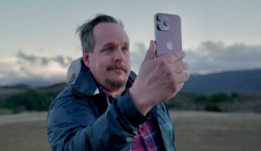 A man holding an iPhone 14 Pro outdoors on a remote hillside