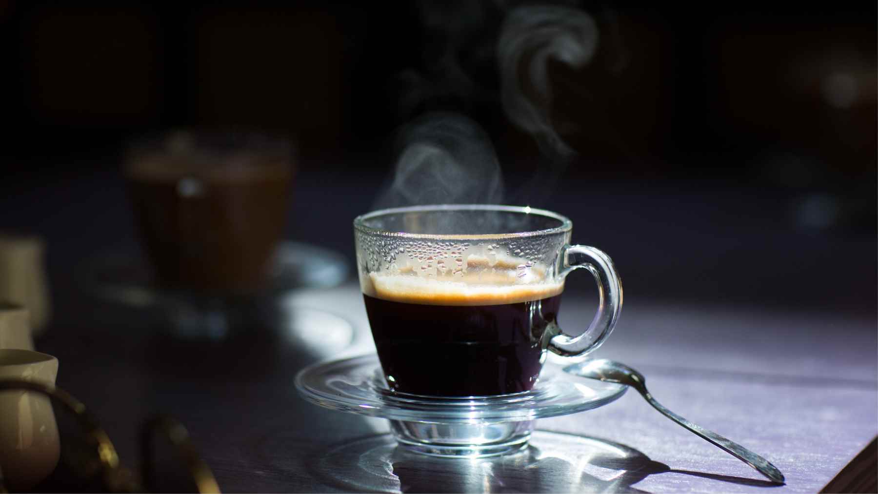 Steaming cup of black coffee in a glass mug on a saucer, illustrating heat loss and the arrow of time.