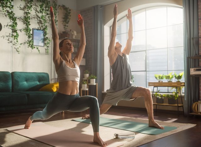 Athletic Young Couple Exercising Together, Stretching and Doing Yoga in the Morning in Bright Sunny Room at Home. Beautiful Man and Woman in Sports Clothes Practising Different Asana Poses on the Mat.