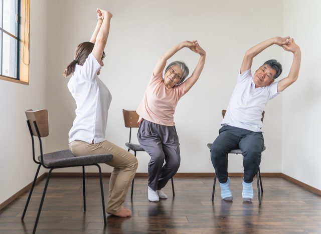 Seniors and elderly men and women doing chair exercises, exercise and rehabilitation at a nursing facility, along with physical therapists, caregivers and trainers