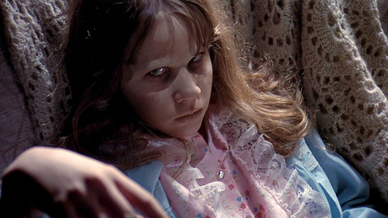 Close-up of Linda Blair as Regan, grinning with white pasty face with scrapes on it in The Exorcist