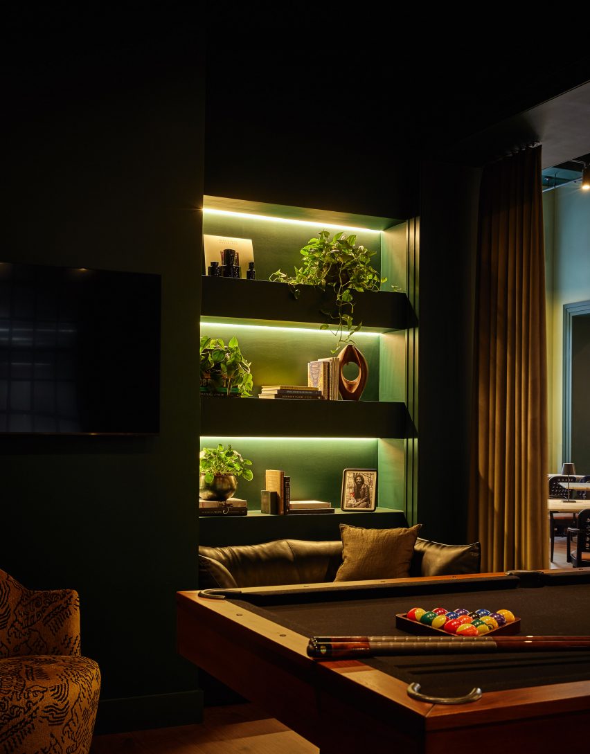 A pool table and large TV screens within a dark green lounge