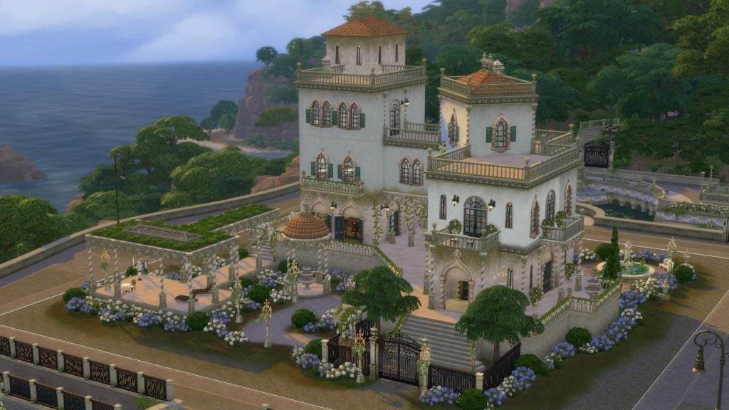 A grand Mediterranean-style villa with terraced balconies, arched windows, and lush gardens sits on a coastal cliff overlooking the ocean.