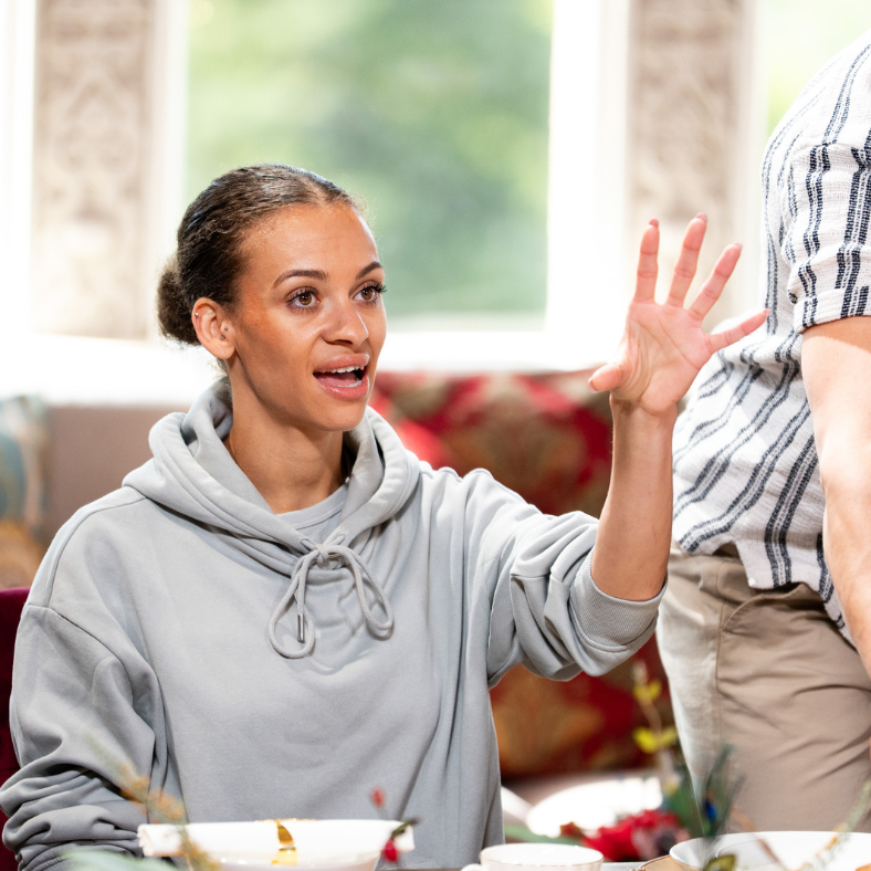 person gesturing at a dining table during a gathering