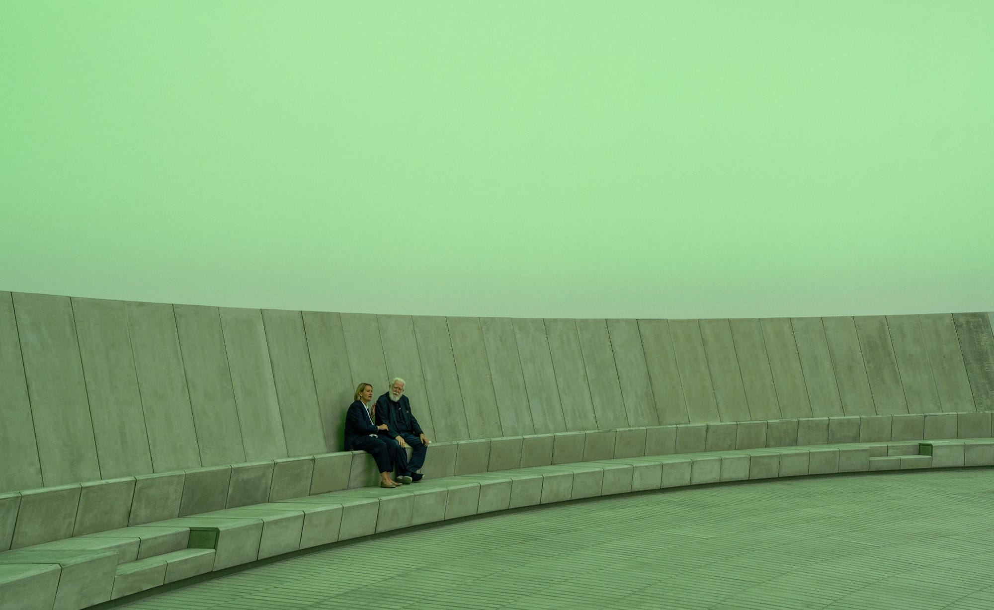 James Turrell and another individual sitting inside of his 'Skyspace' artwork at ARoS as it is illuminated green