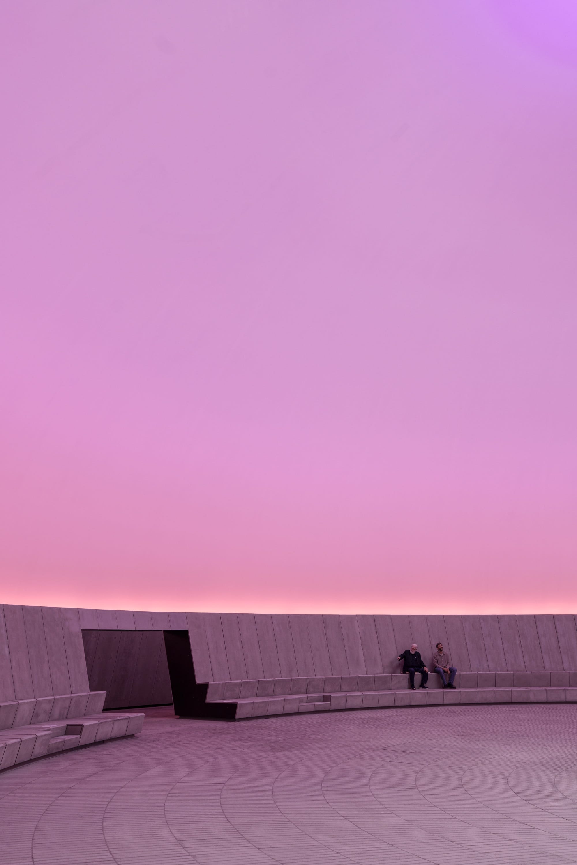 James Turrell and another individual sitting inside of his 'Skyspace' artwork at ARoS as it is illuminated pink