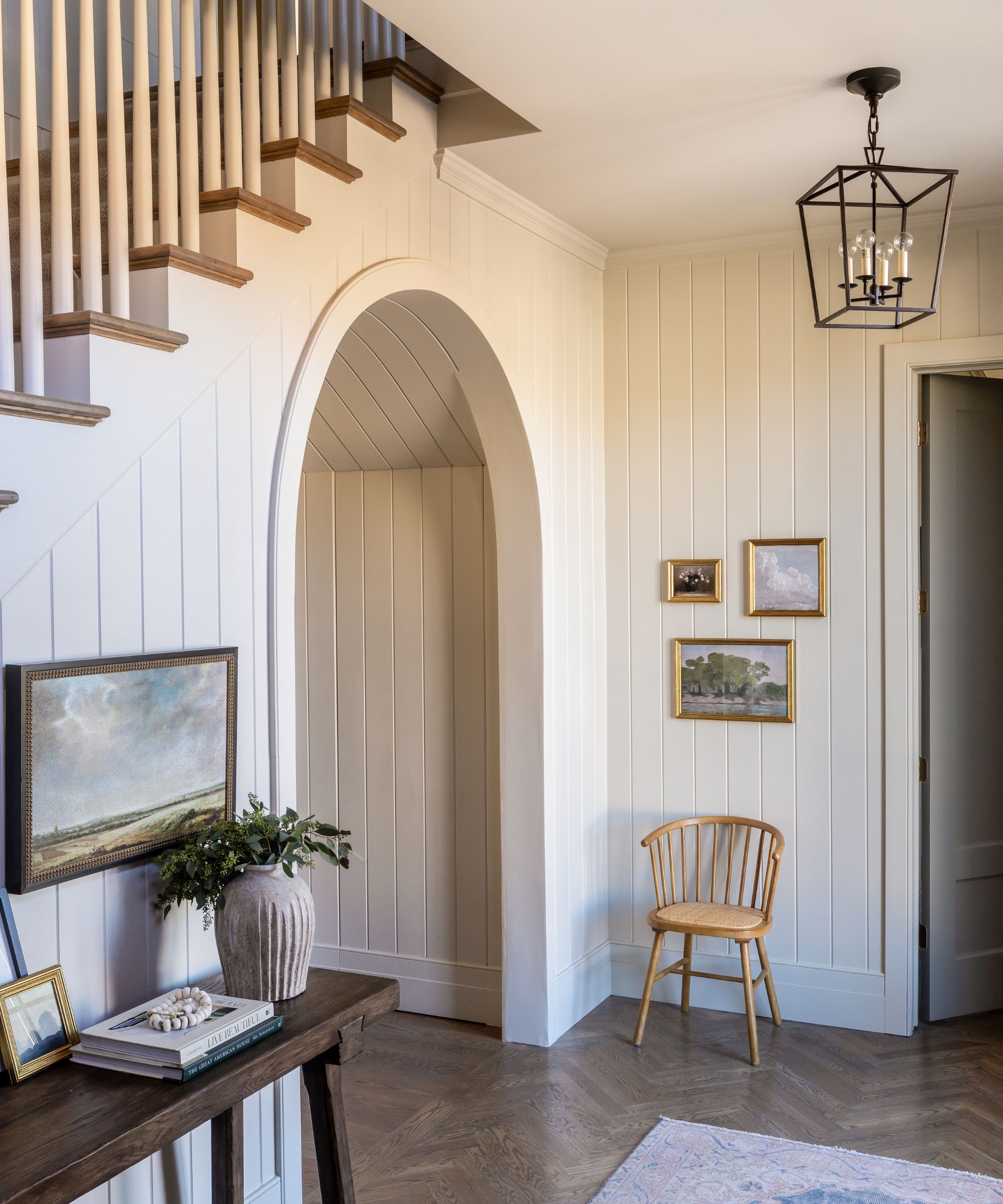 A warm white hallway with paneled walls, a wooden floor, and gold-framed art on the walls