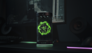 The Project AVA desk companion from Razer sits atop a black desk. A holographic image of Razer's logo lights up the screen in green.
