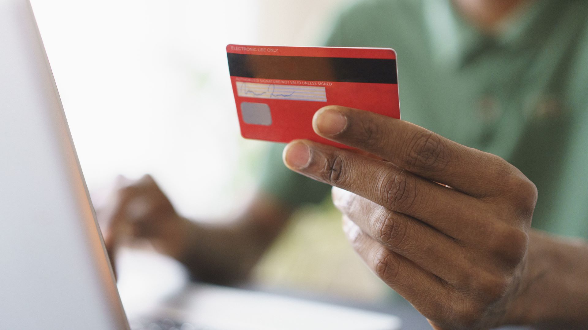 Cropped image of man holding credit while shopping online through laptop at home
