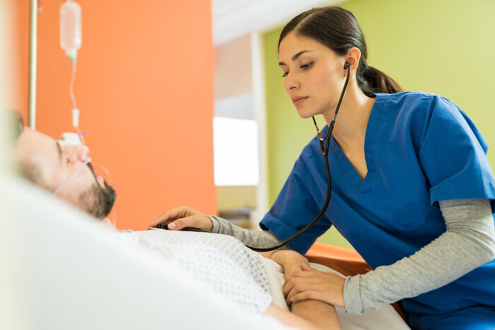 Female nurse in blue scrubs checking patient with stethoscope in hospital room about patients leaving against medical advice