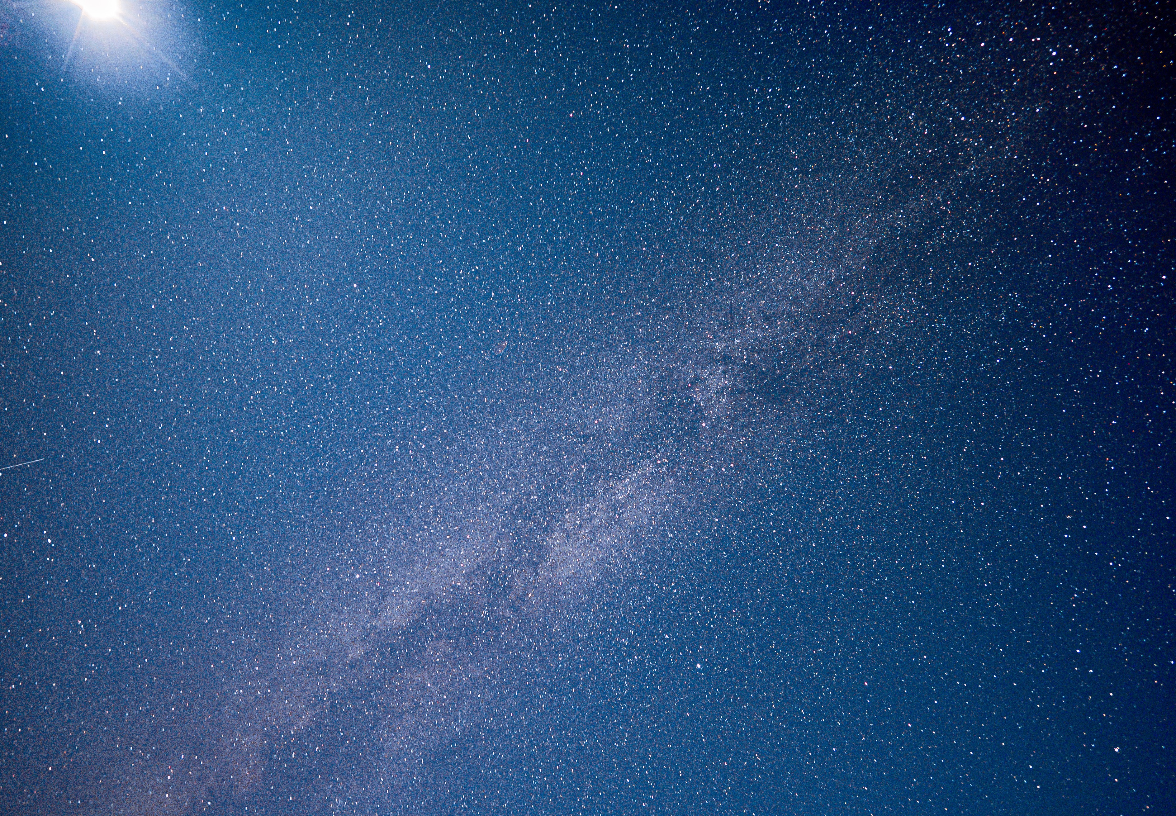 milky way stretches through the center of the image and a bright near-full moon shines in the upper left corner.