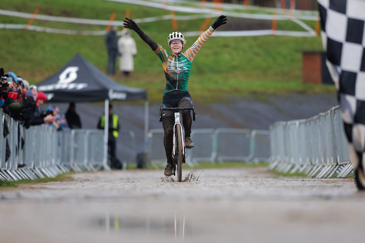Woman crosses finish line on a bike with arms in the air