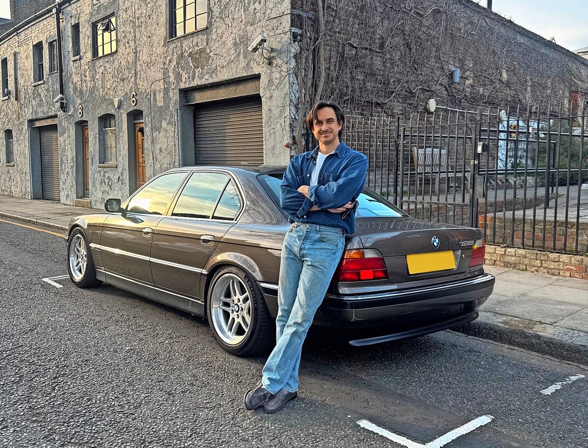 Michal Fidowicz posing next to a parked car on a street.