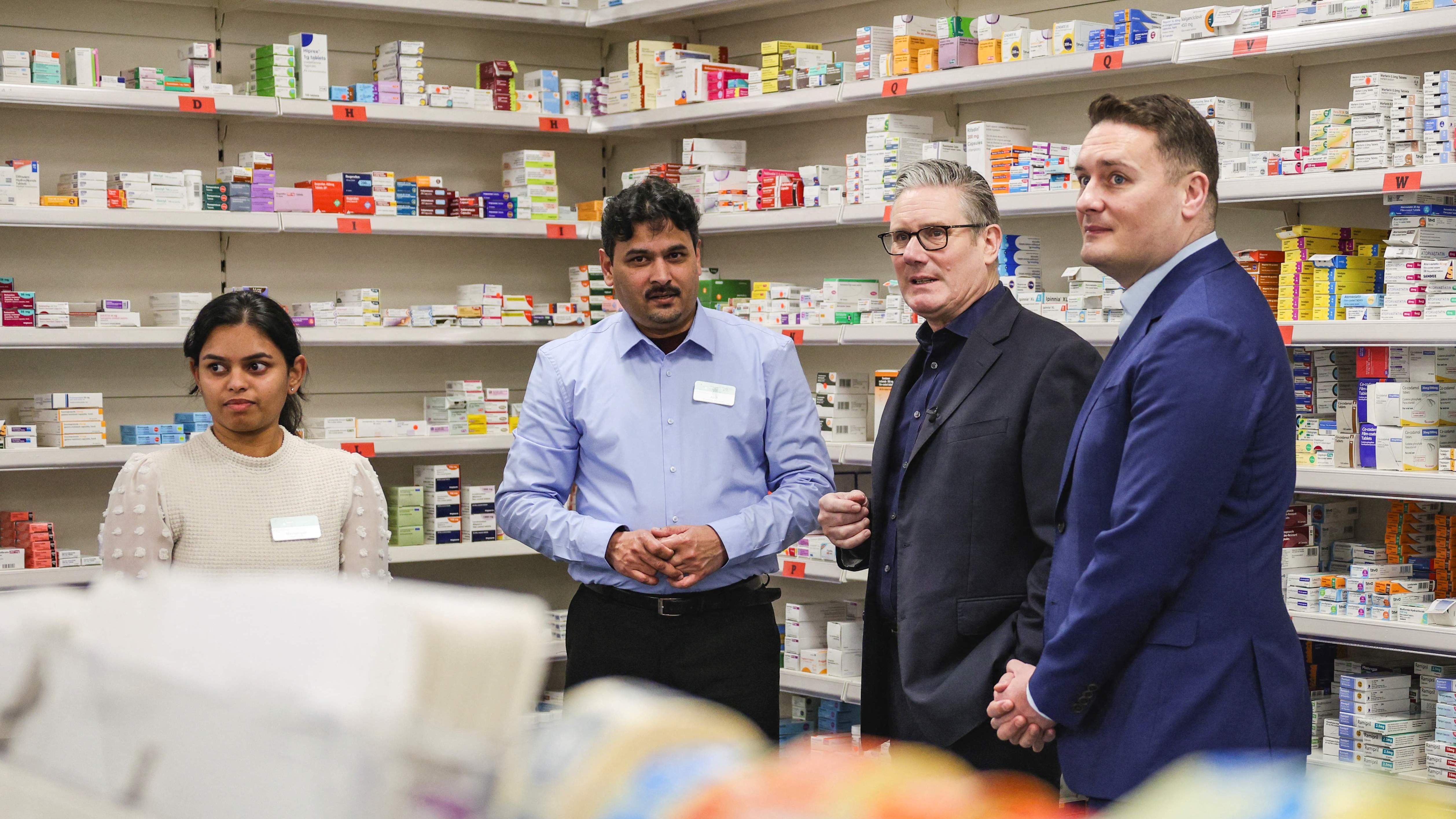 Keir Starmer and Wes Streeting speak with pharmacist Mahendranathan Mayoorigah and pharmacy manager Abdul Abid in a pharmacy.