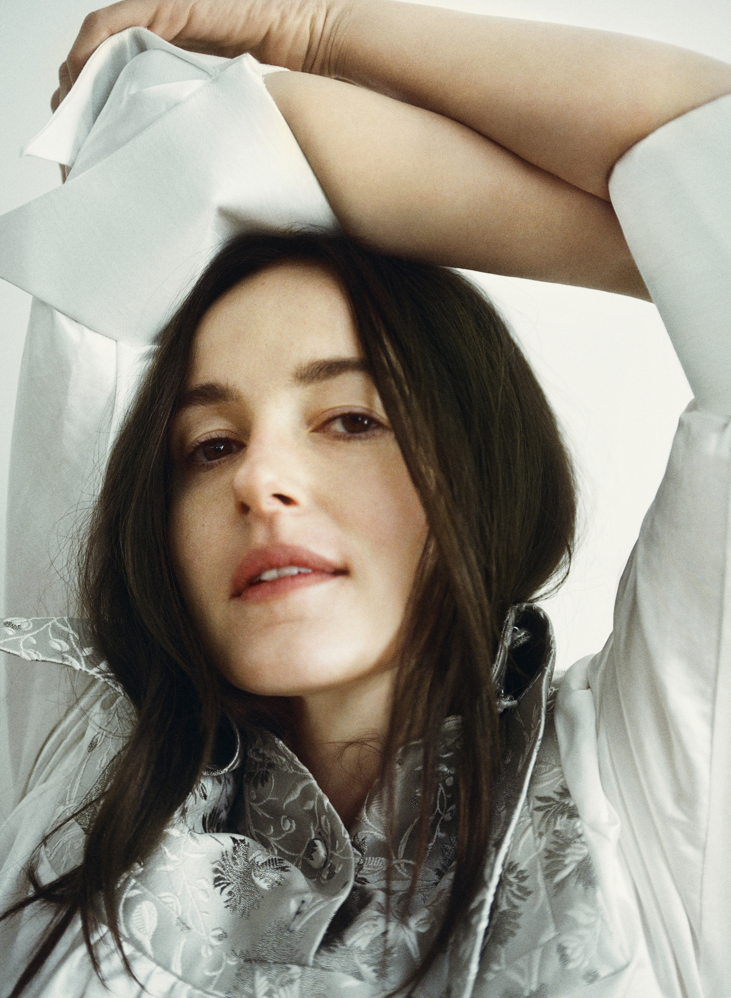 Renate Reinsve looking up at the camera with her arms raised, wearing a white shirt.