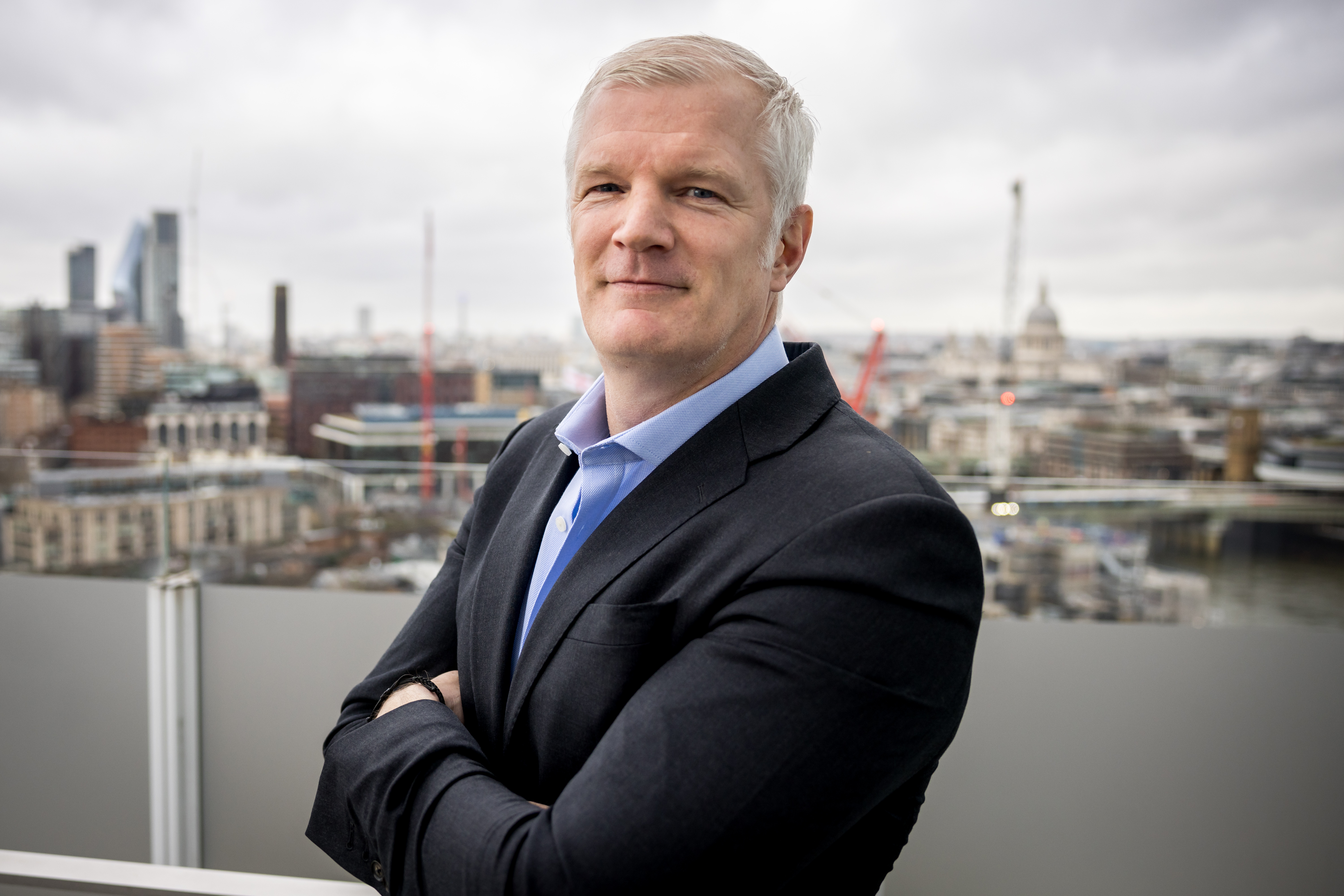 Armed forces minister Al Carns poses for a portrait on a balcony with a city skyline in the background.
