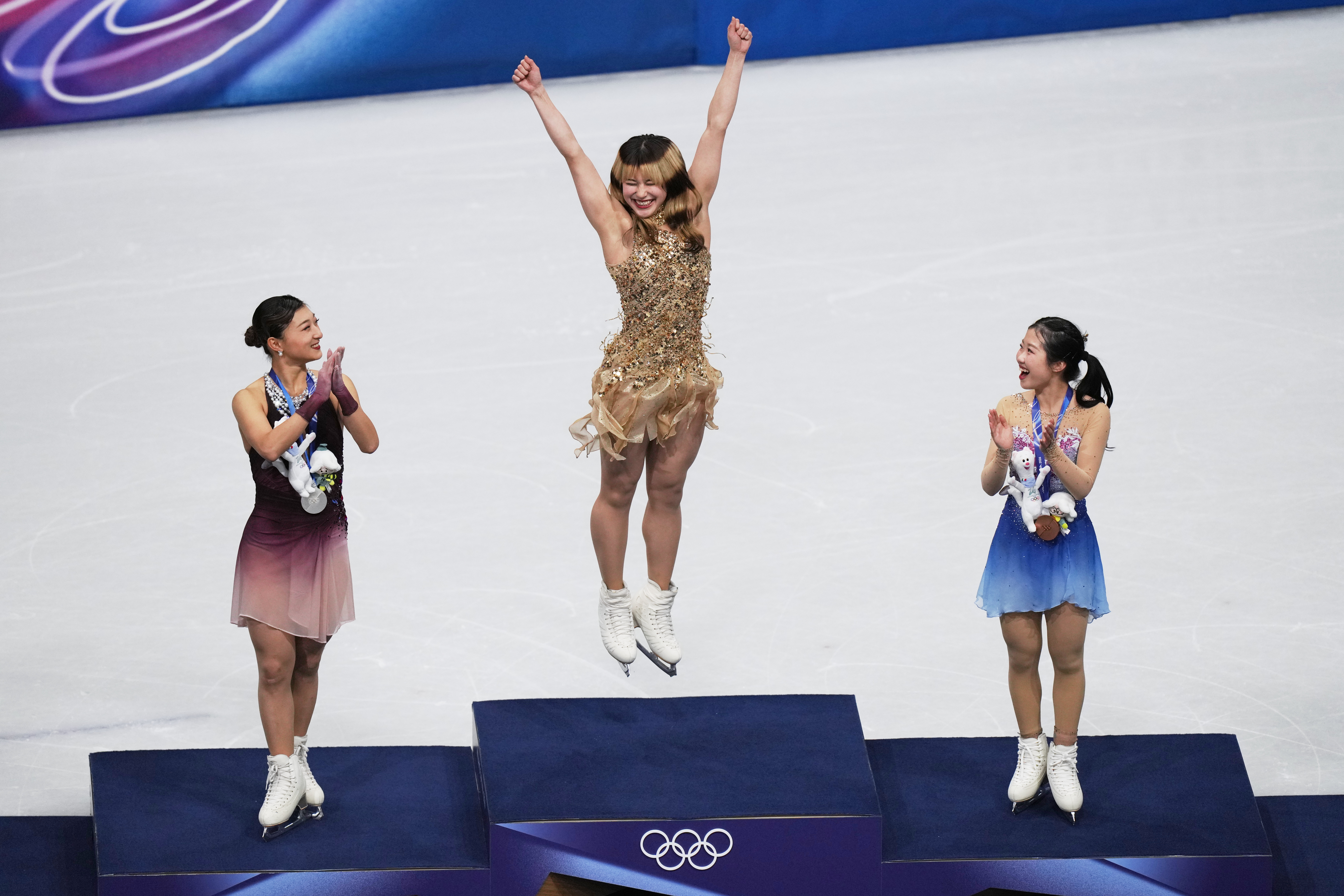 Kaori Sakamoto, Alysa Liu, and Ami Nakai celebrating on the podium after the women's free skate program at the 2026 Winter Olympics.