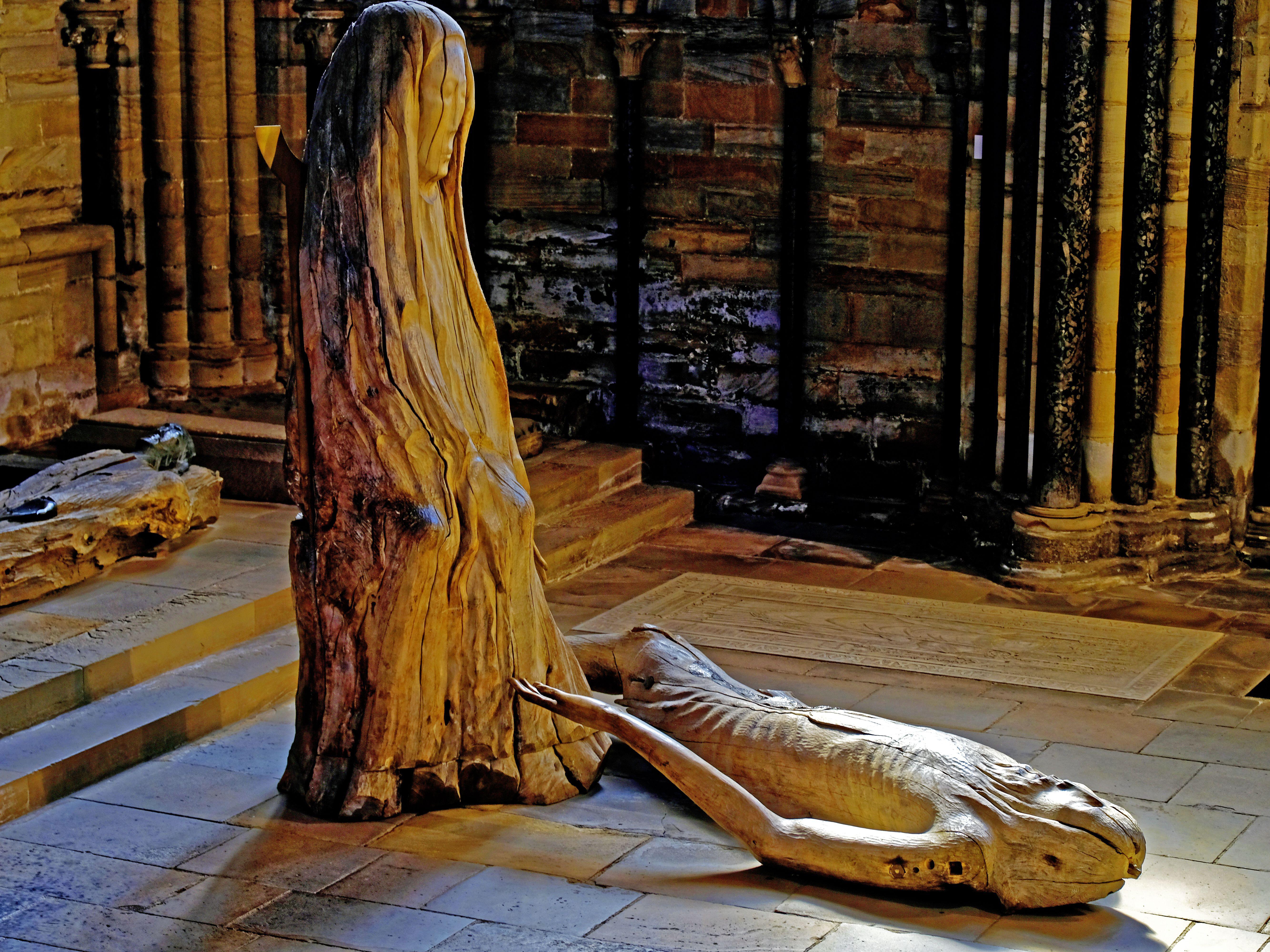 Wooden sculpture of the Pieta by Fenwick Lawson ARCA, depicting a standing robed figure and a reclining figure, in Durham Cathedral.