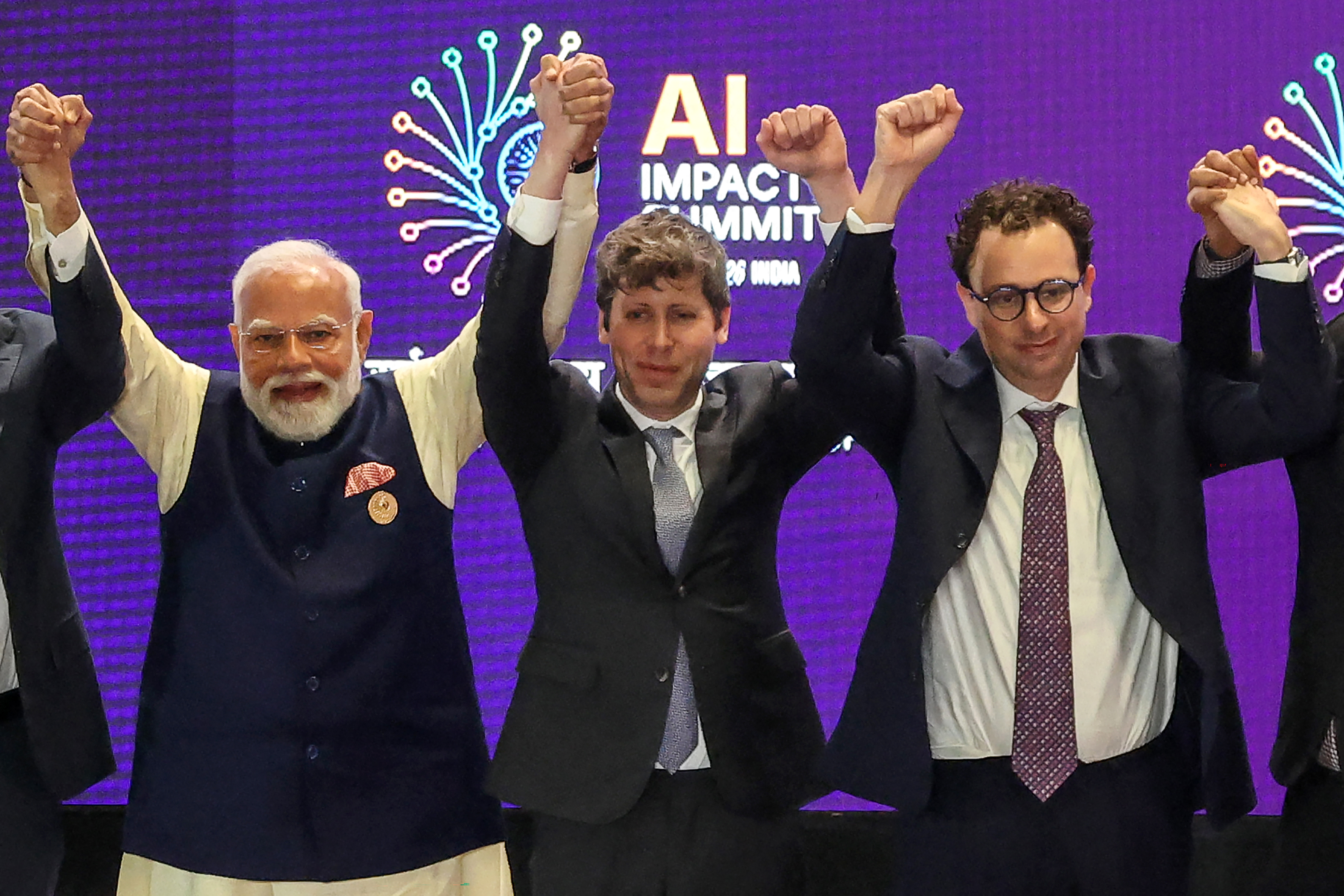 Prime Minister Narendra Modi, OpenAI CEO Sam Altman, and Anthropic CEO Dario Amodei raising their joined hands in a group photo.
