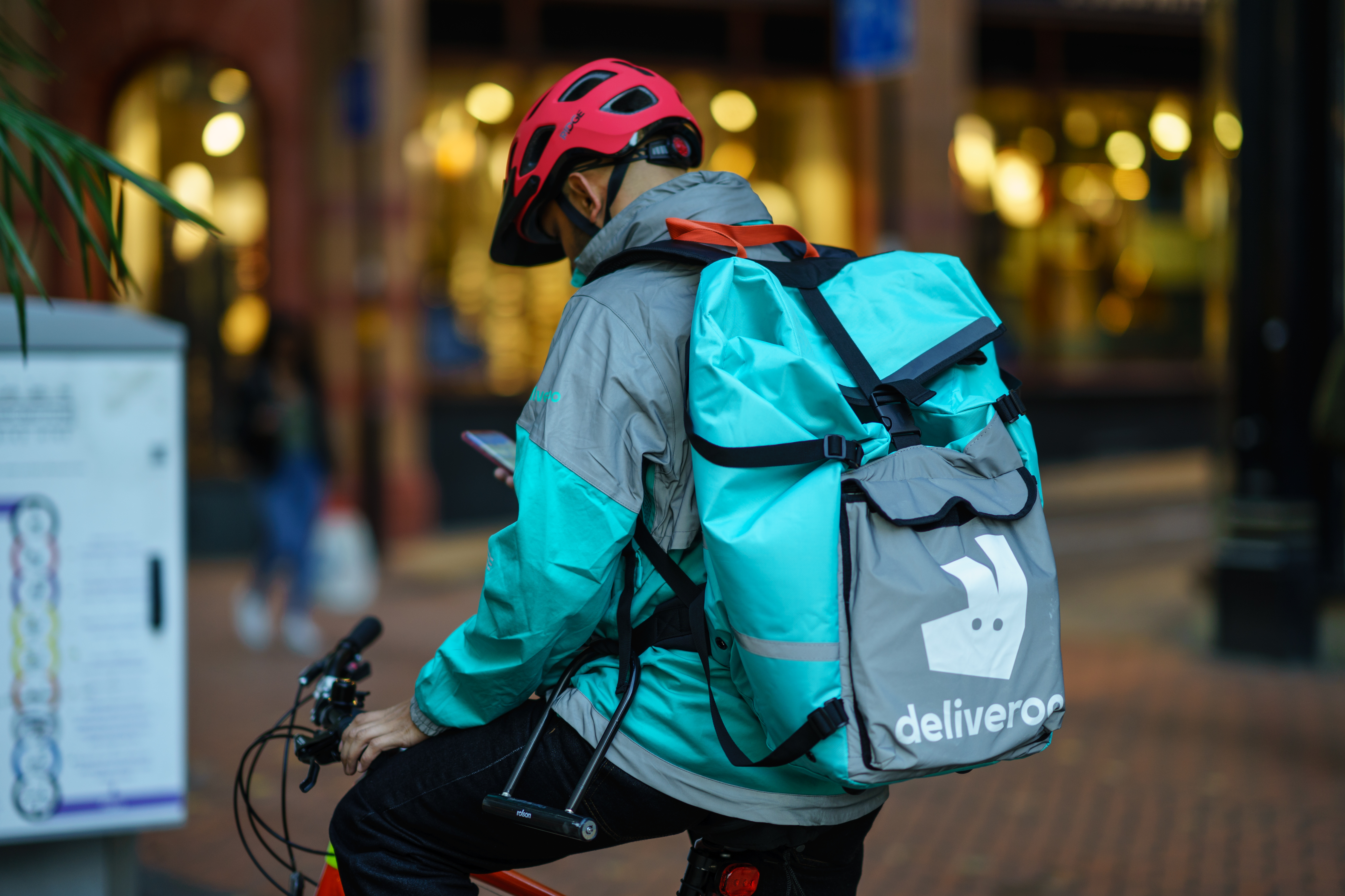 A Deliveroo food delivery person on a bicycle checks their mobile phone.