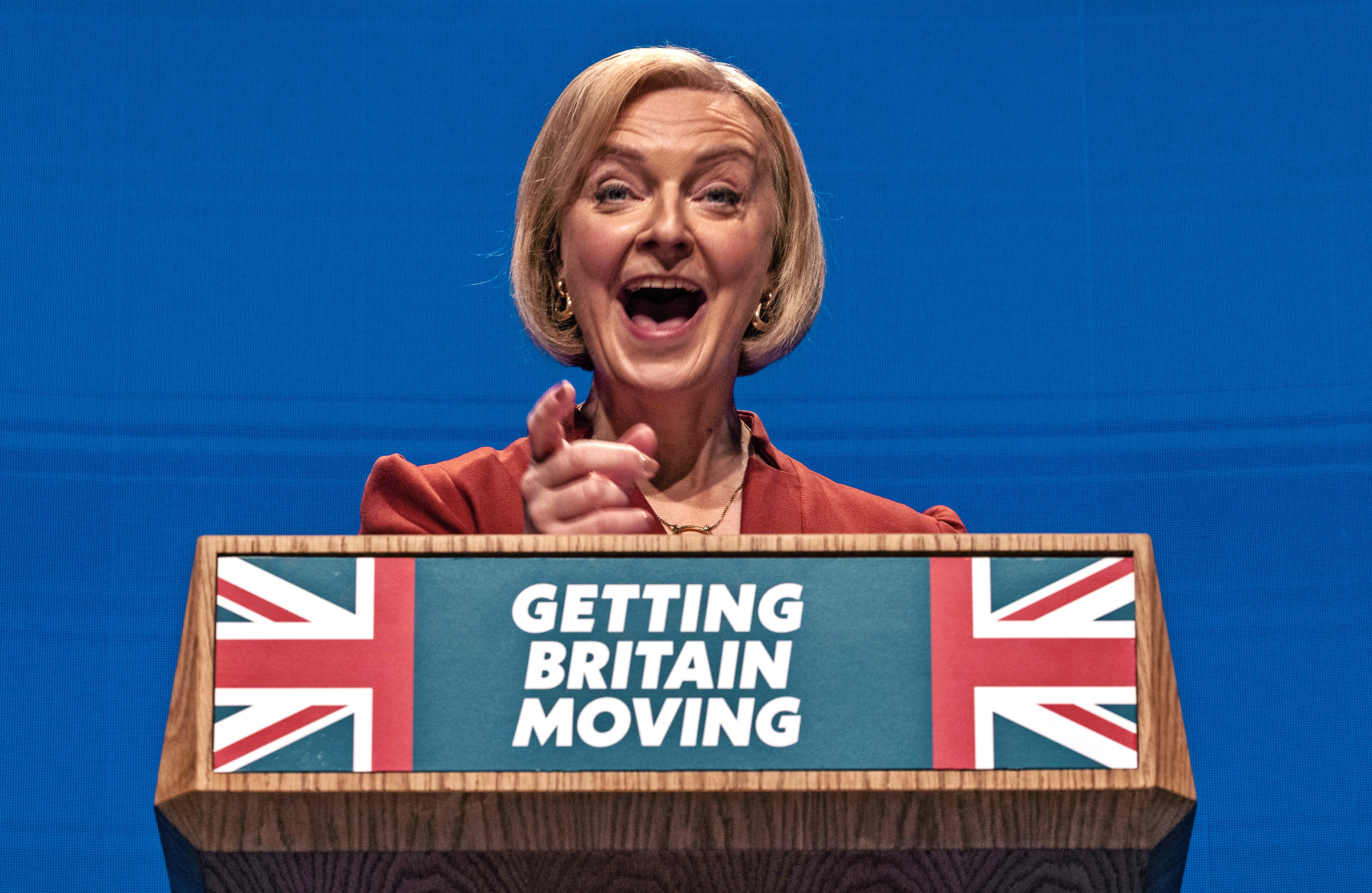 Prime Minister Liz Truss speaking at a podium with a Union Jack and the text "GETTING BRITAIN MOVING".
