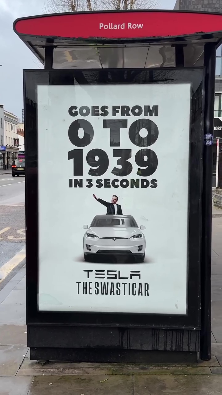 Illustration of a bus stop advertisement showing Elon Musk giving a Nazi salute from a Tesla, with text "GOES FROM 0 TO 1939 IN 3 SECONDS" and "TESLA THE SWASTICAR".