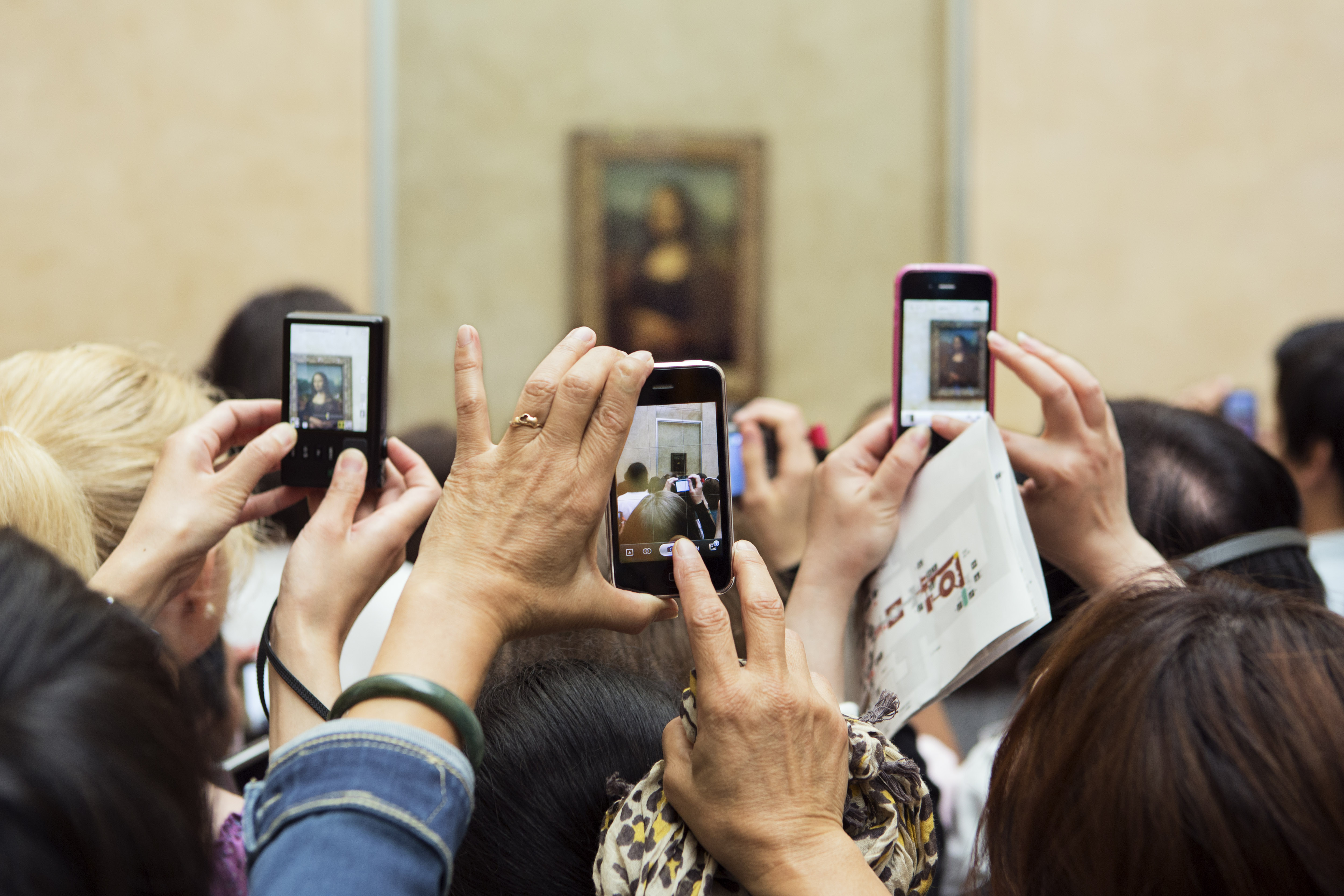 Visitors taking photos of the Mona Lisa painting with their phones at the Louvre Museum.