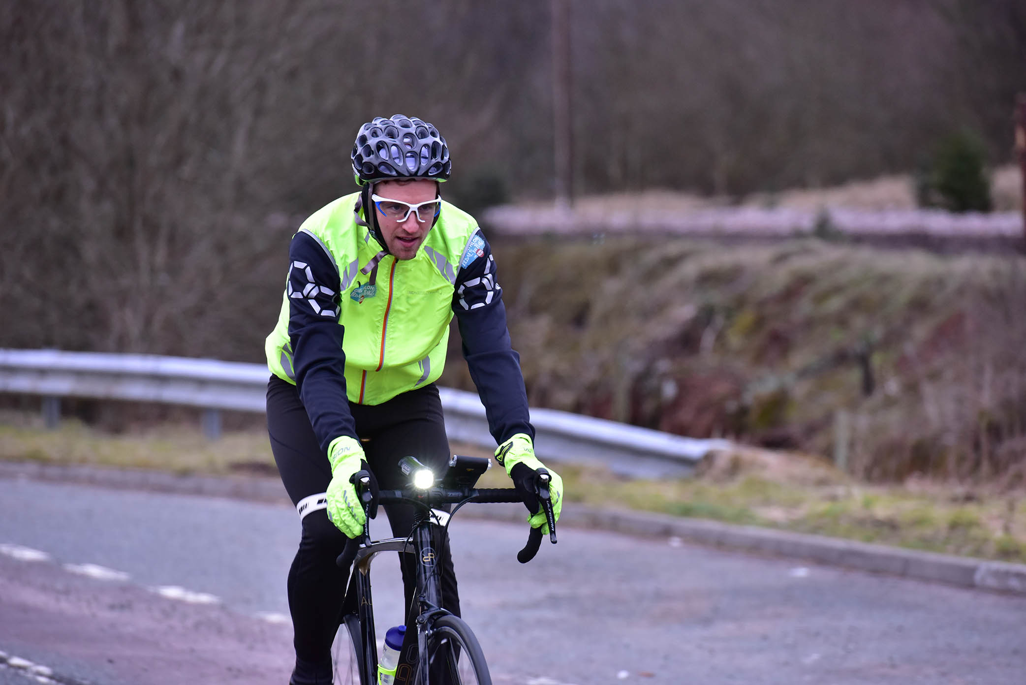 Greg James cycling in a bright yellow jacket, black pants, helmet, and white glasses for Sport Relief.