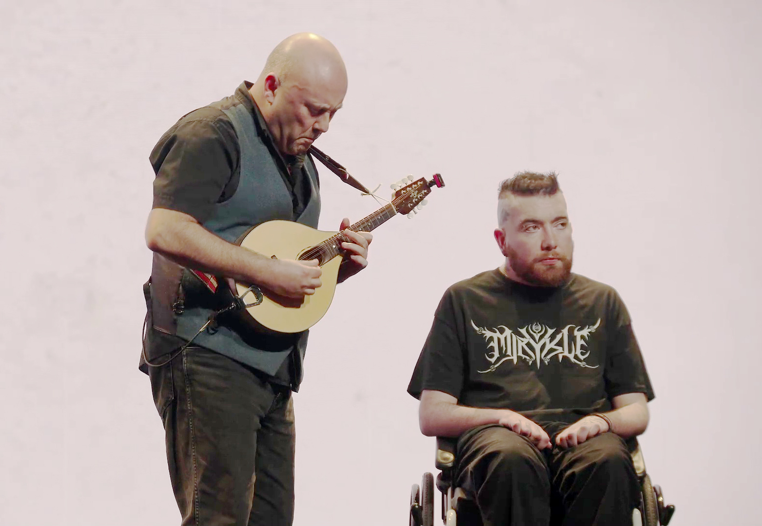 Patrick Darling playing a mandolin next to Nick Cocking in a wheelchair.