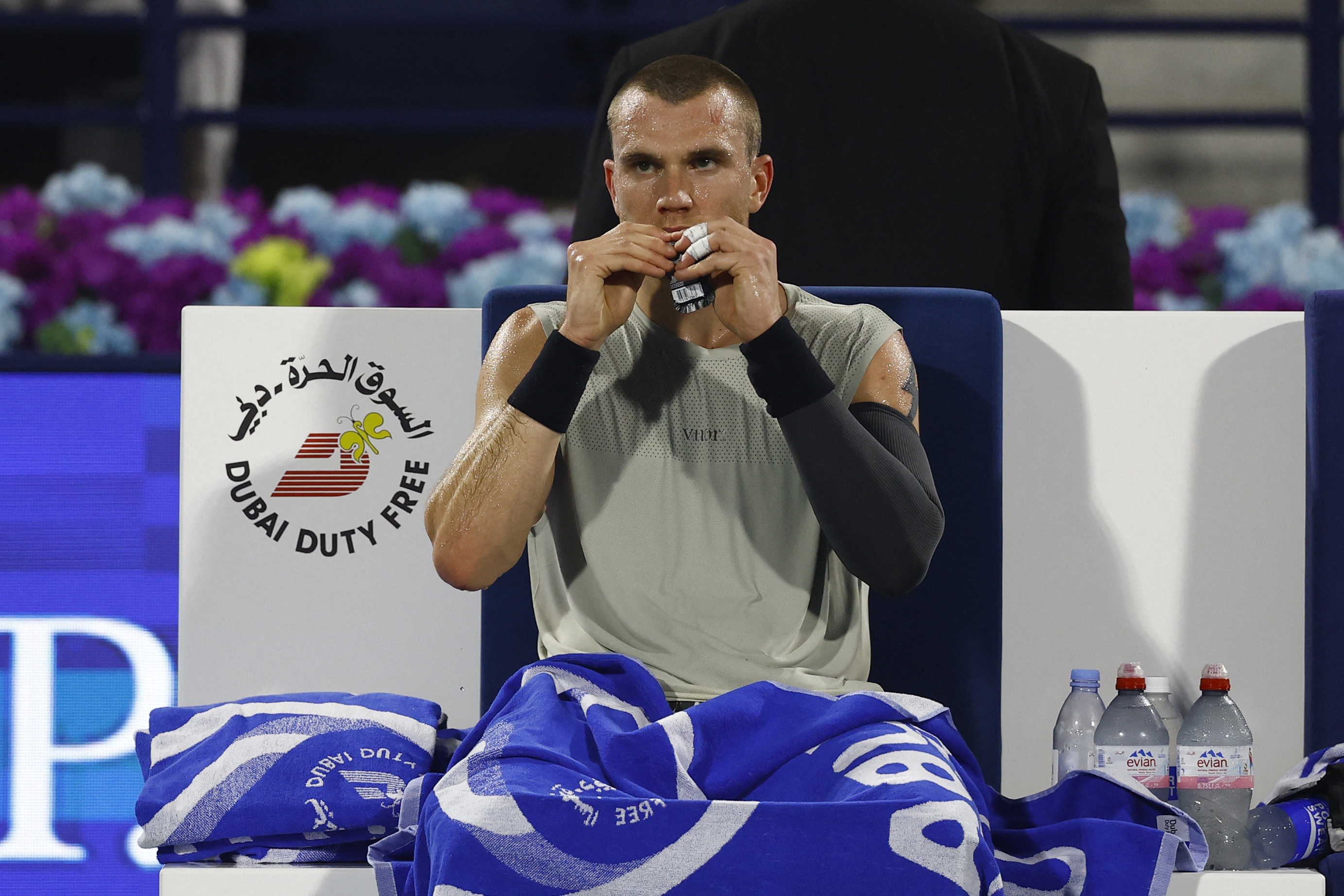 Britain's Jack Draper unwrapping something while sitting during his match at the Dubai Tennis Stadium.