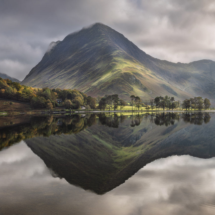 A mountain reflected in a still lake, with a line of trees along the shore and autumn foliage on the hillside.