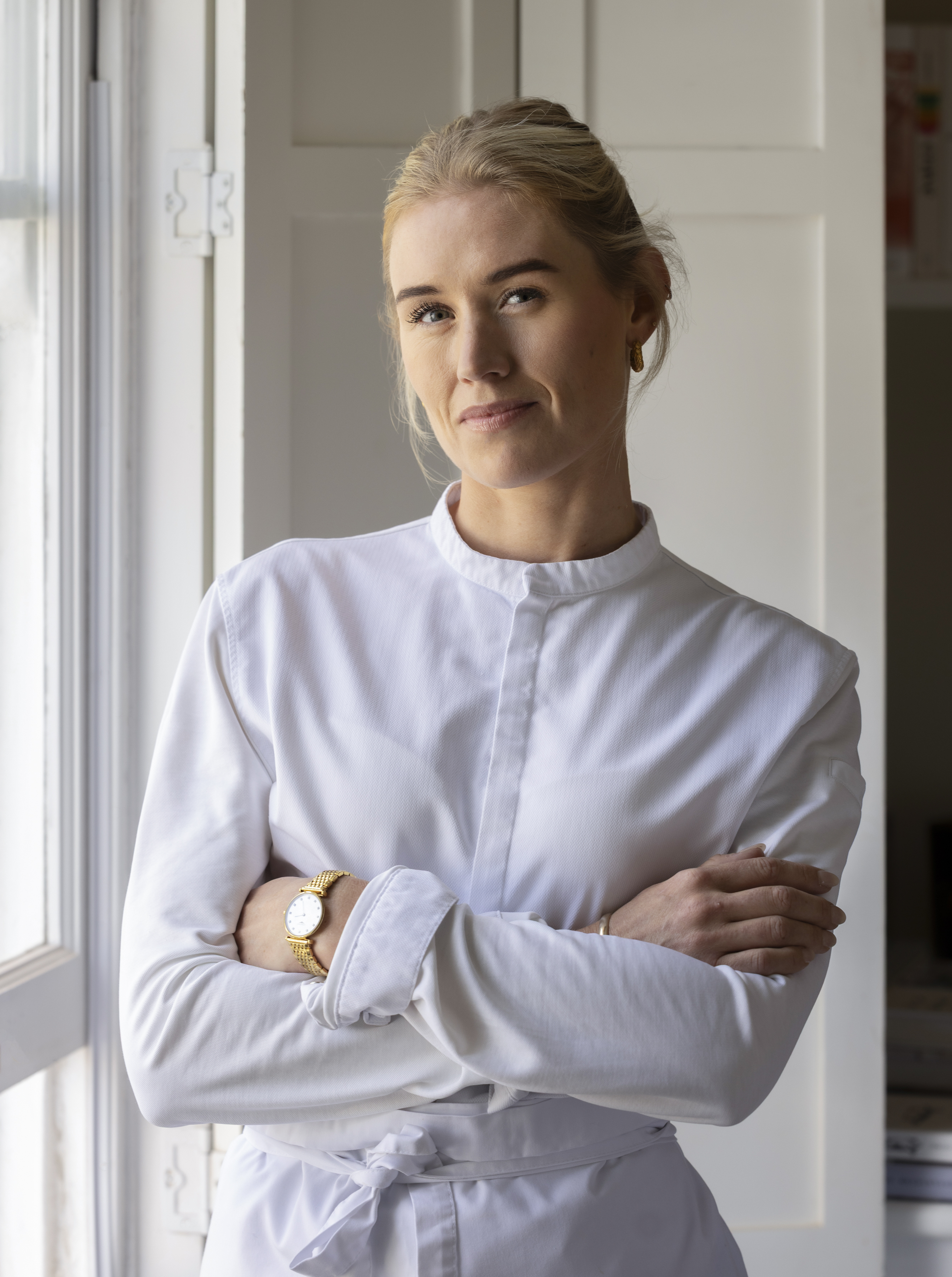 Portrait of Kate Austen, a blonde woman wearing a white chef's coat, standing with her arms crossed.