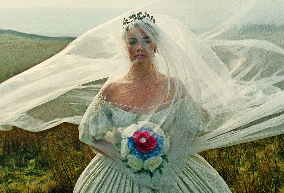 Margot Robbie as Catherine Earnshaw in “Wuthering Heights” wearing a wedding gown and veil with a bouquet of red, white, and blue flowers.