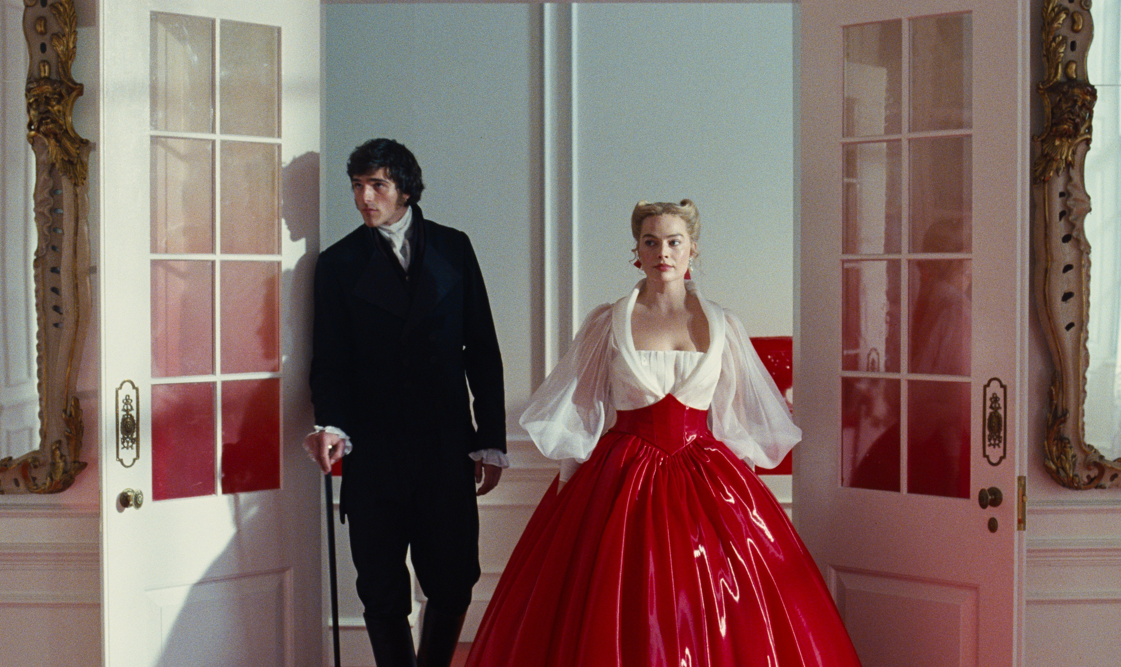 A man in a black coat and a woman in a red gown with a white top standing in a doorway.