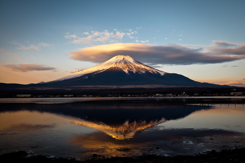 Snow-capped Mount Fuji reflecting in a lake at sunset.