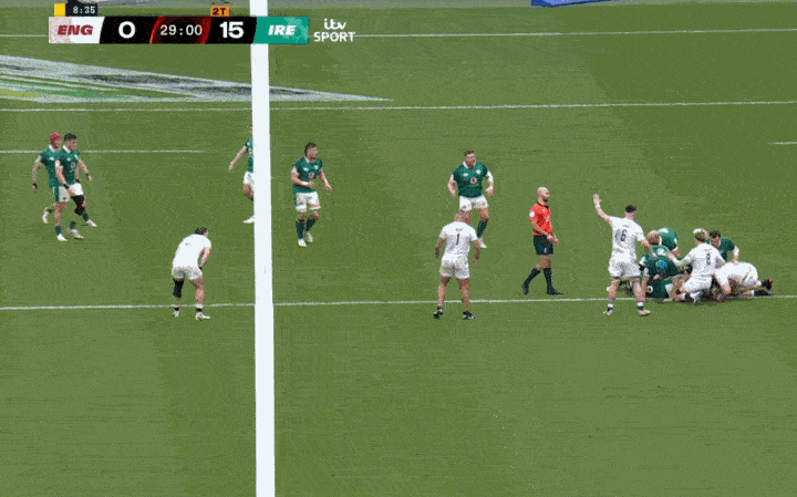 Rugby players in white and green jerseys in a scrum on a green field.