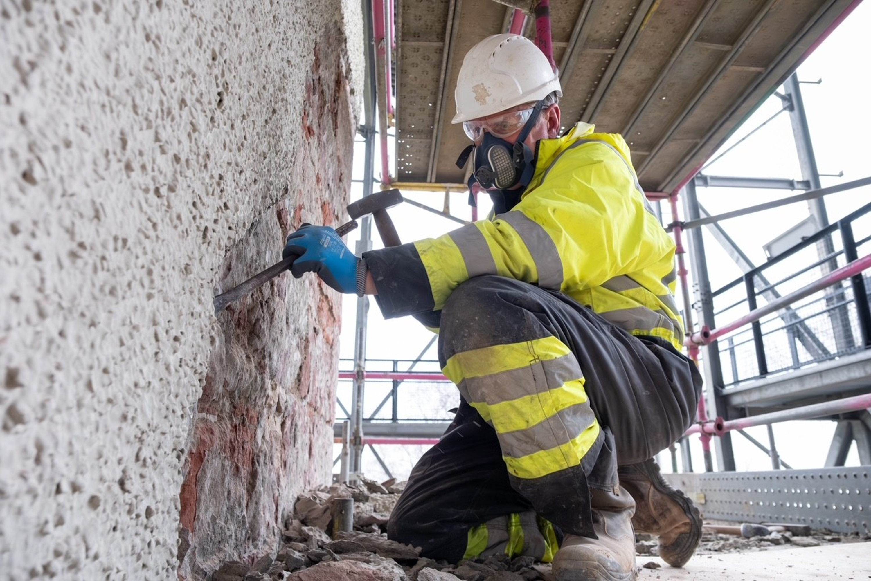 A stonemason removing render from a stone wall at The Hill House.