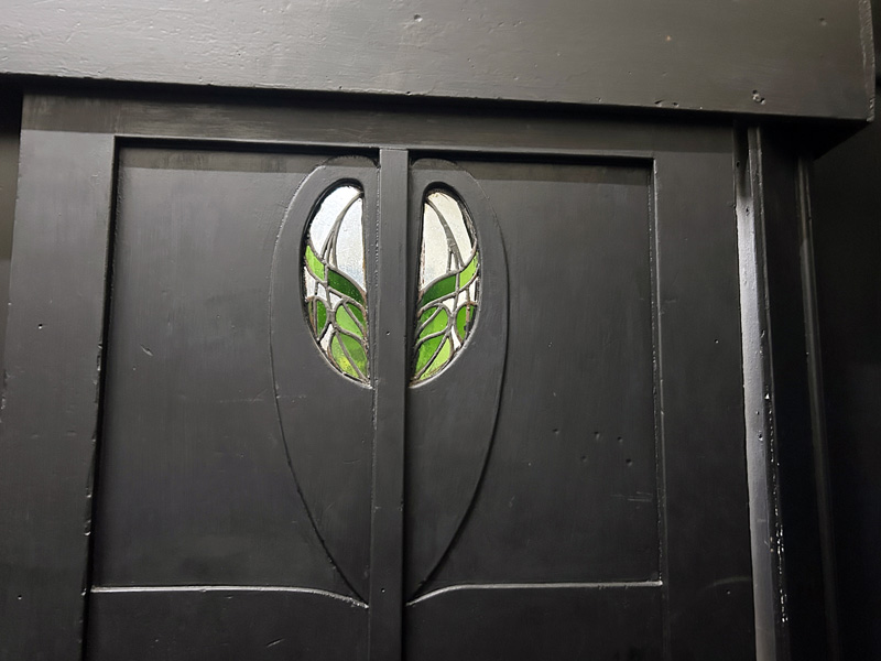 Black wooden double doors with art nouveau stained glass.