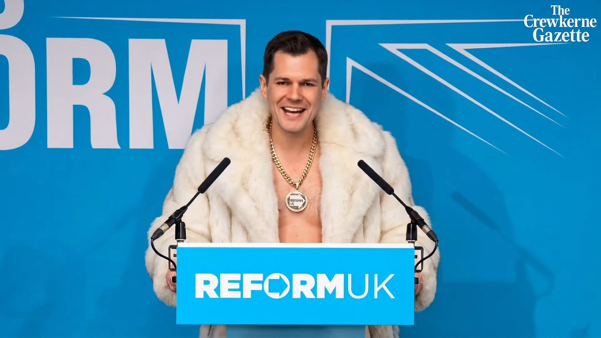 A smiling man wearing a white fur coat and a large gold chain with a medallion, standing at a podium with "REFORM UK" written on it.