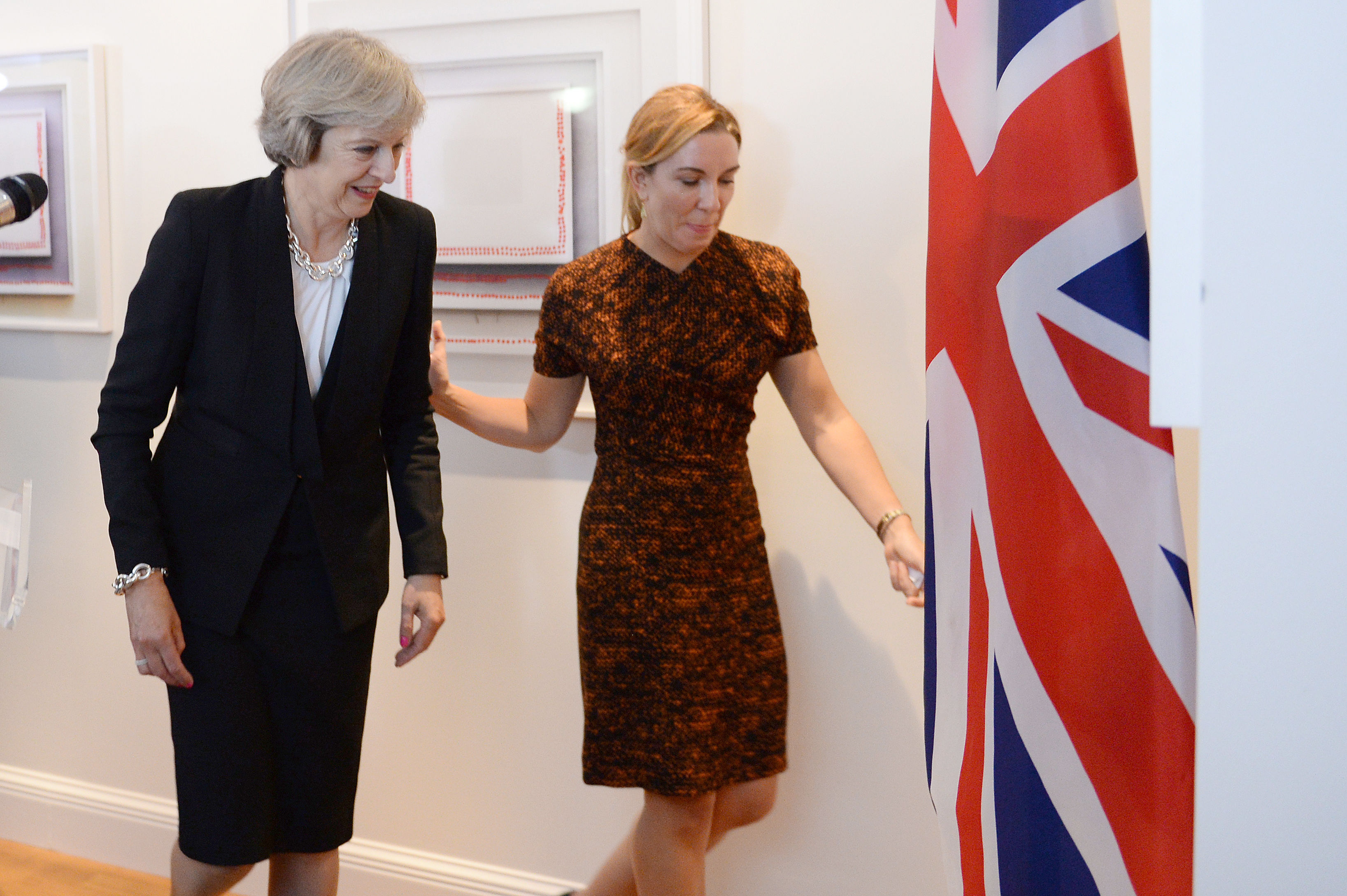 Theresa May and Antonia Romeo walking past a Union Jack flag.
