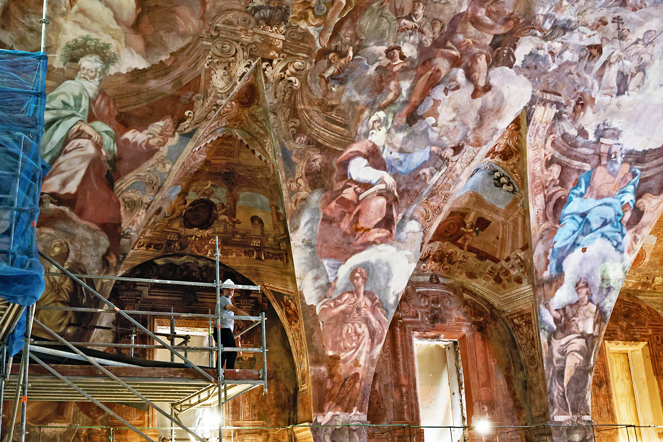 A restorer on scaffolding examines the restored Baroque ceiling murals of the Church of Santos Juanes.