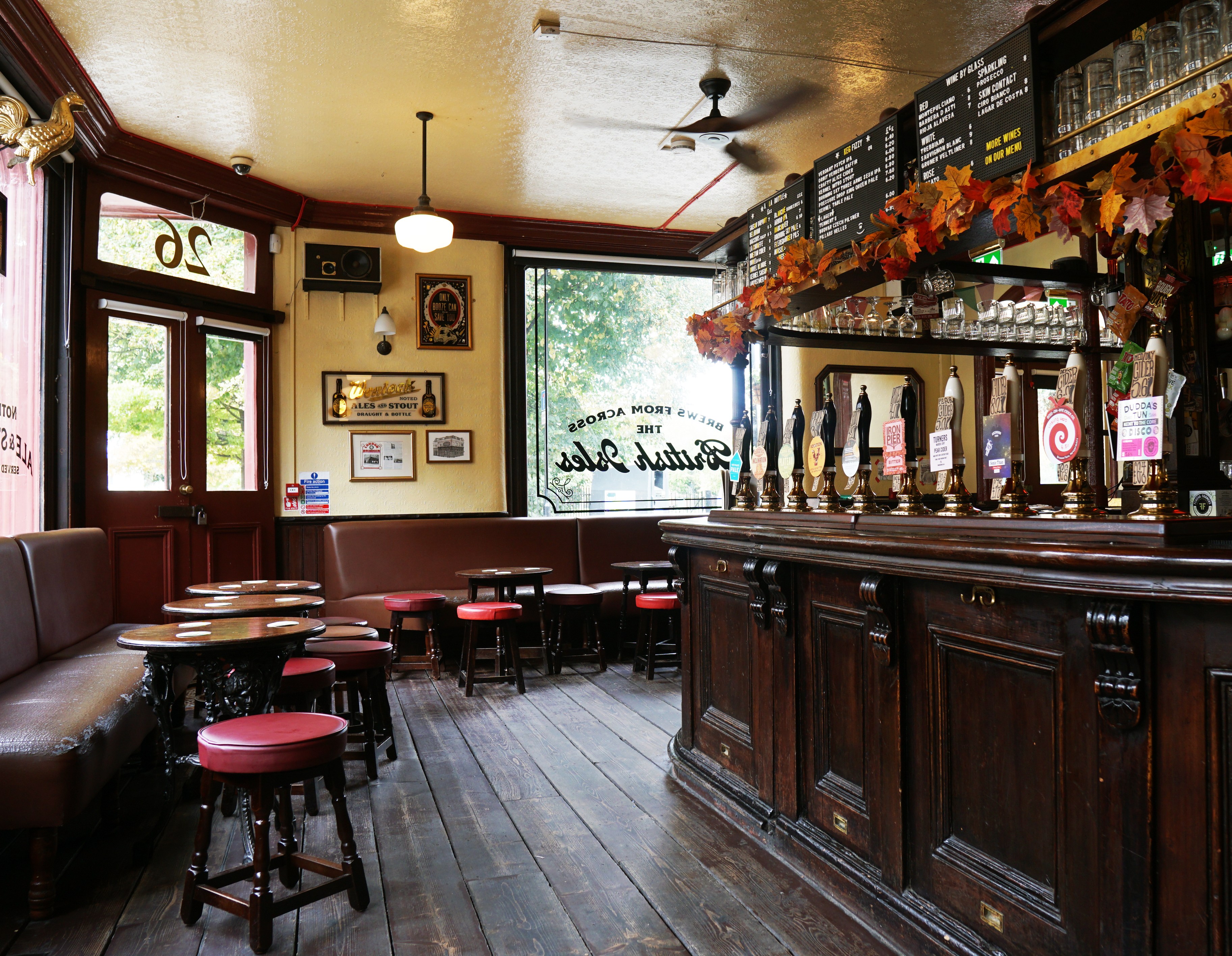 The interior of The Wenlock Arms pub in Hoxton, with wooden floors, a long dark wood bar with beer taps, red bar stools, and booth seating.