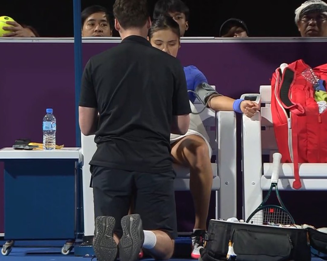 A female tennis player having her blood pressure taken on the sidelines by a kneeling man.