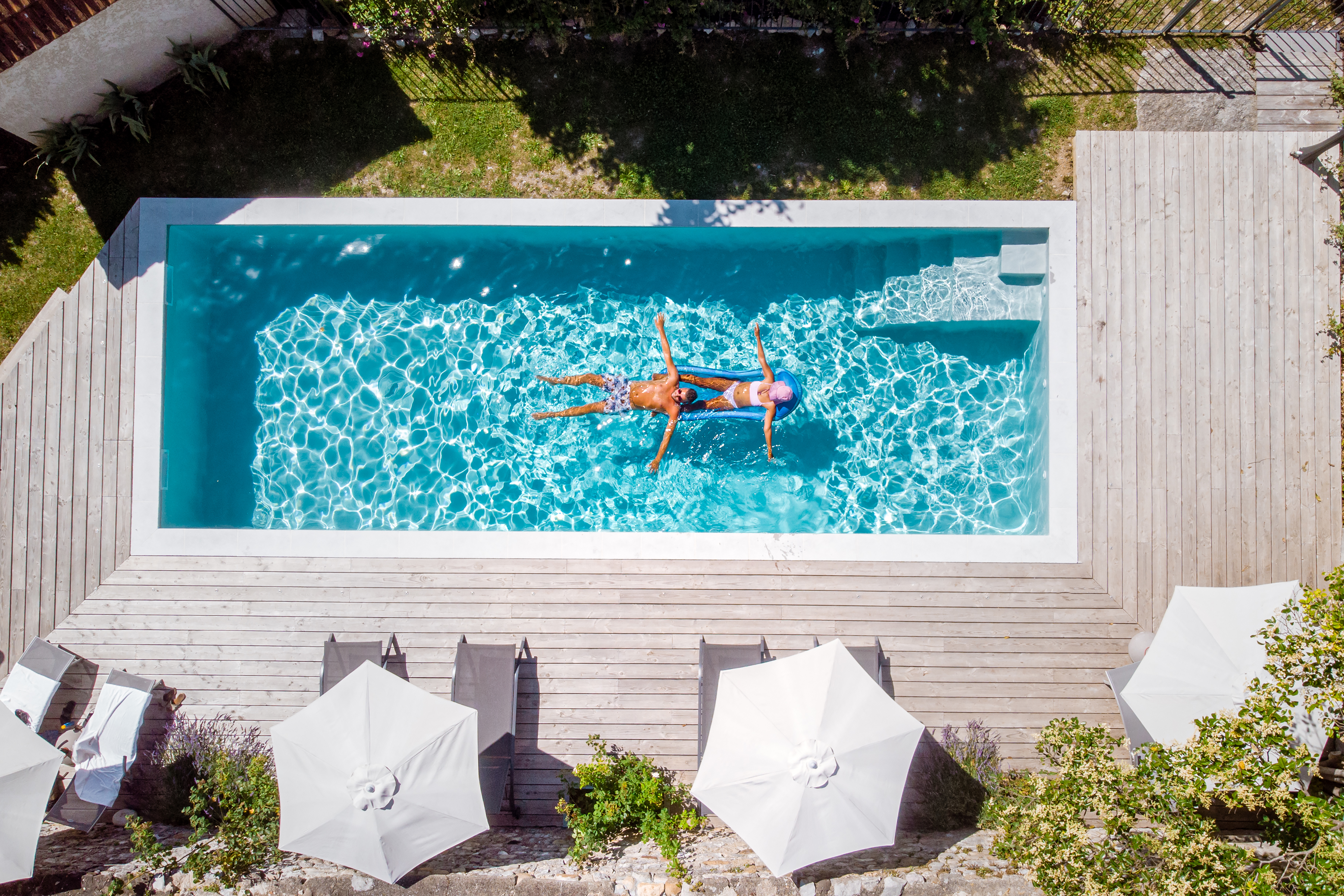 Aerial view of a man and a woman relaxing on inflatable rafts in a swimming pool at a luxury vacation home.