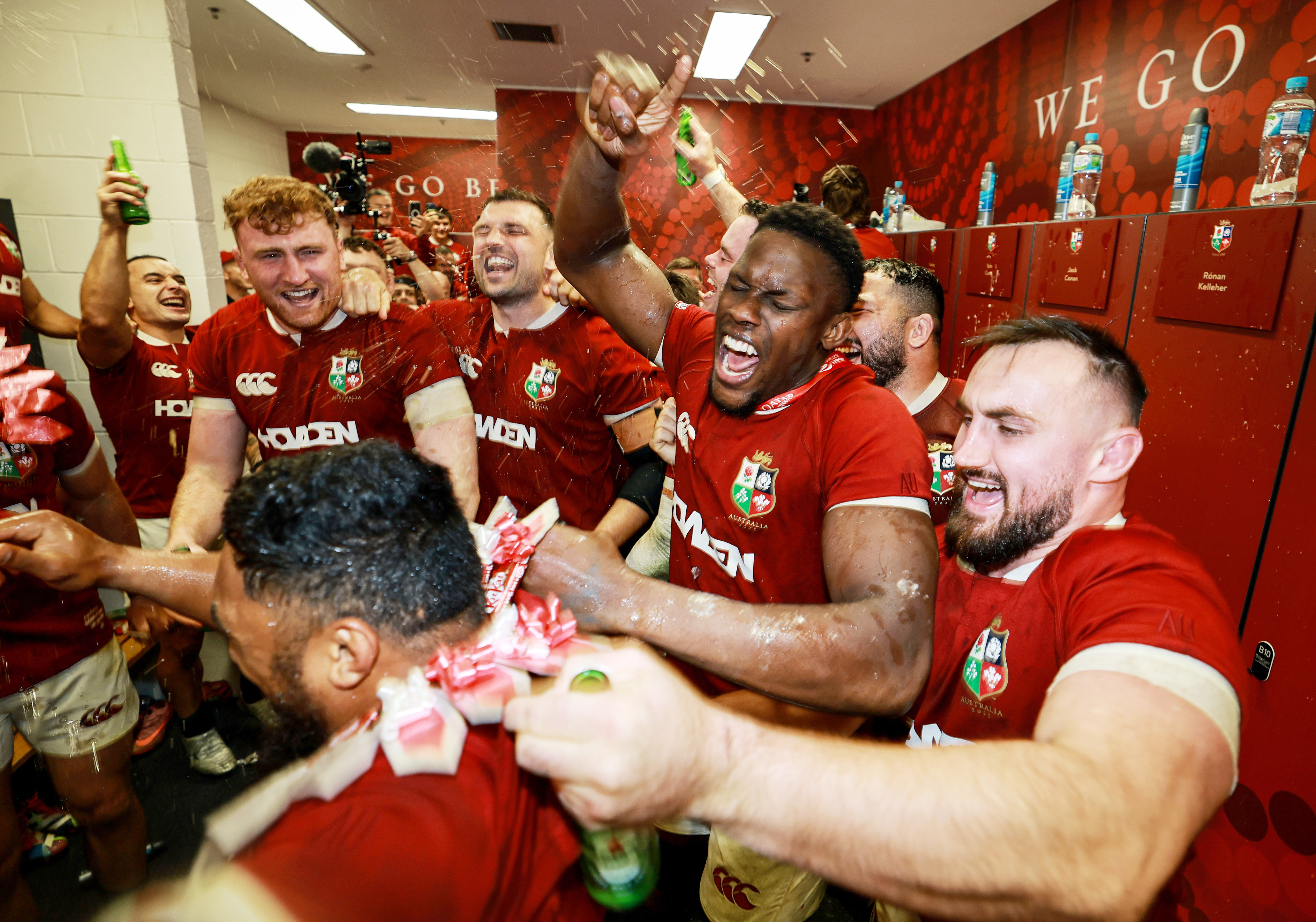 Rugby players celebrate in a locker room, spraying drinks.