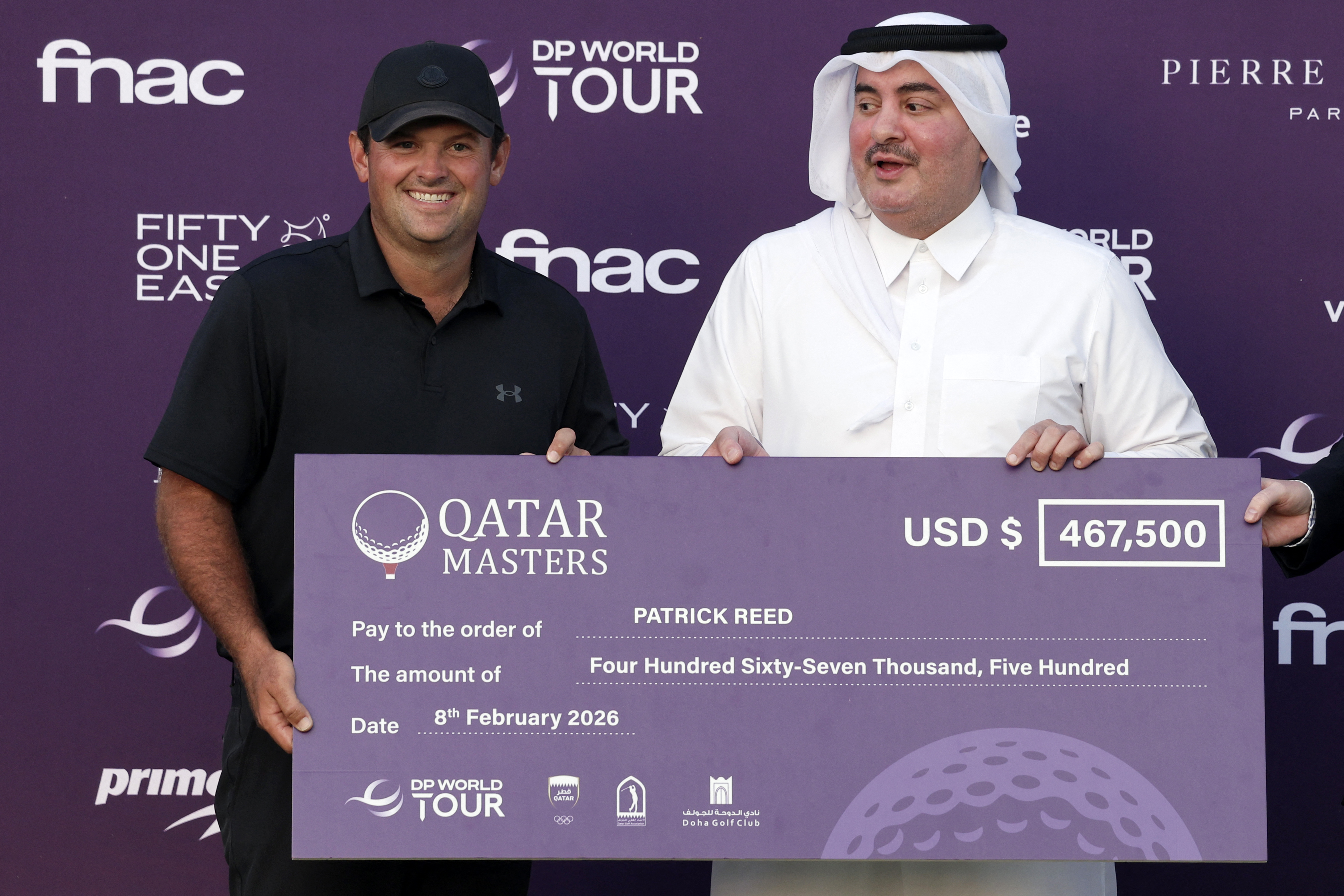 Patrick Reed and a man in traditional Qatari dress hold a large check for $467,500 for Reed's win at the Qatar Masters.