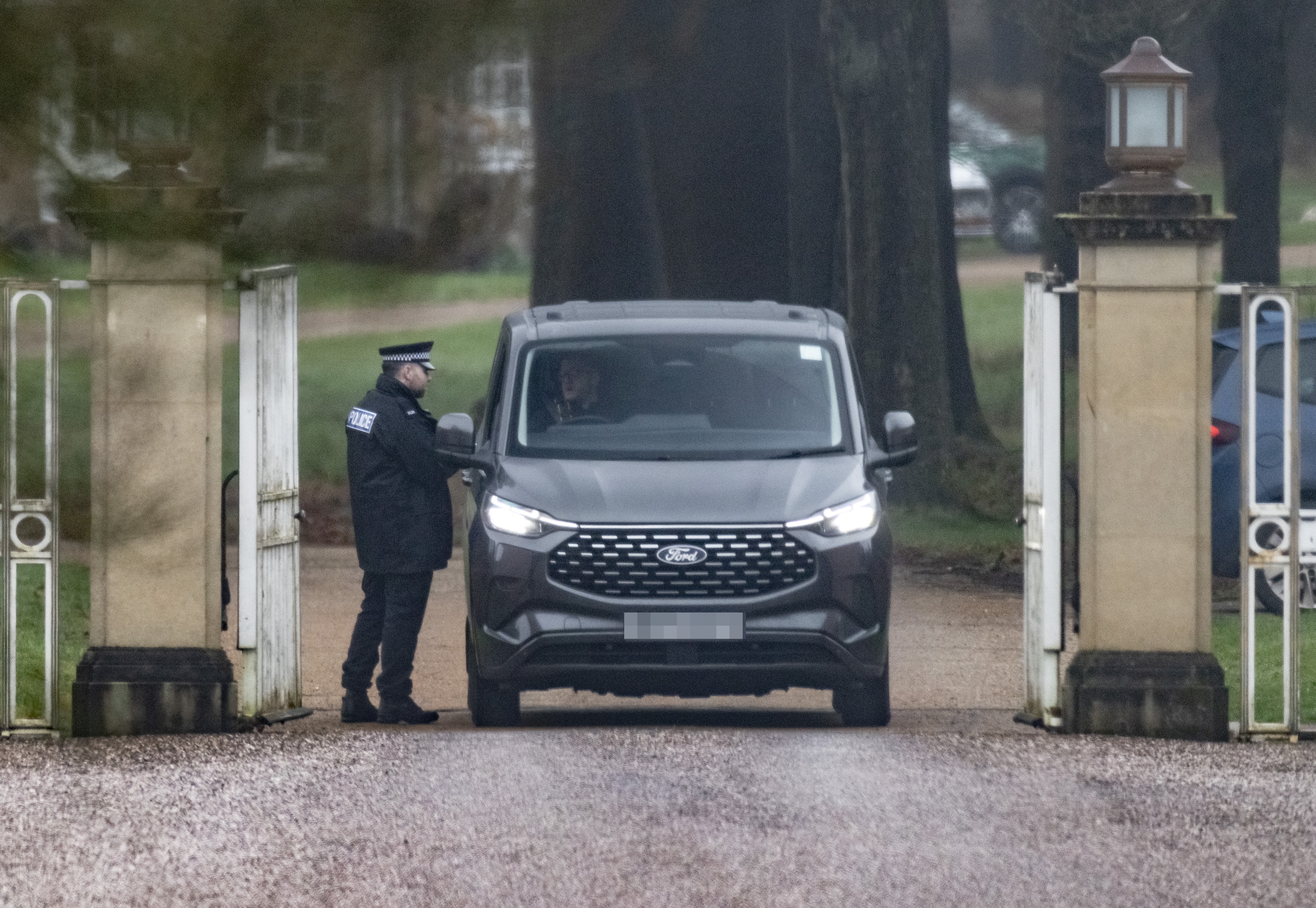 Police officer checking a gray Ford van at the gates of Royal Lodge near Windsor Castle.