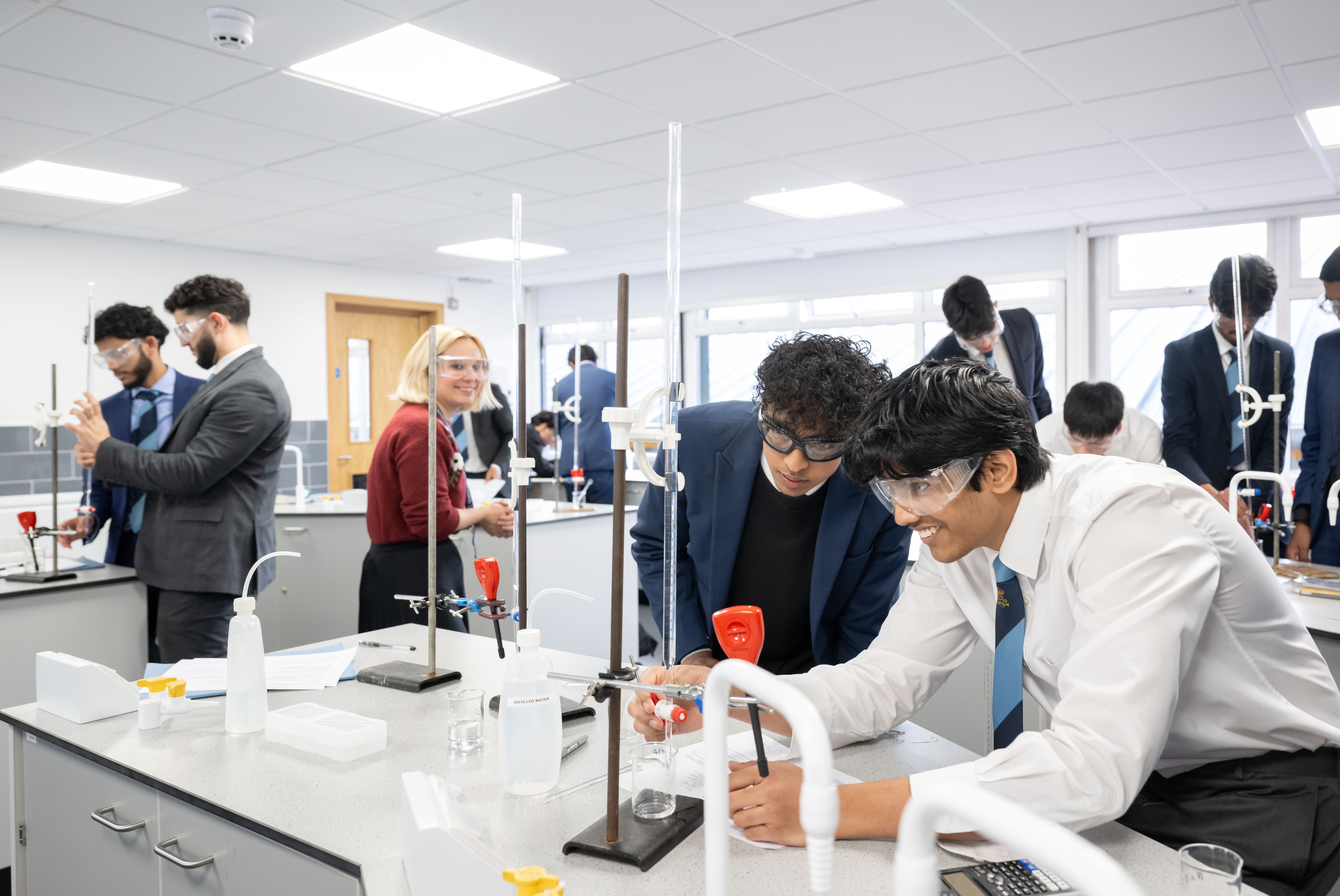 Students in safety glasses conducting a chemistry practical in a refurbished lab.
