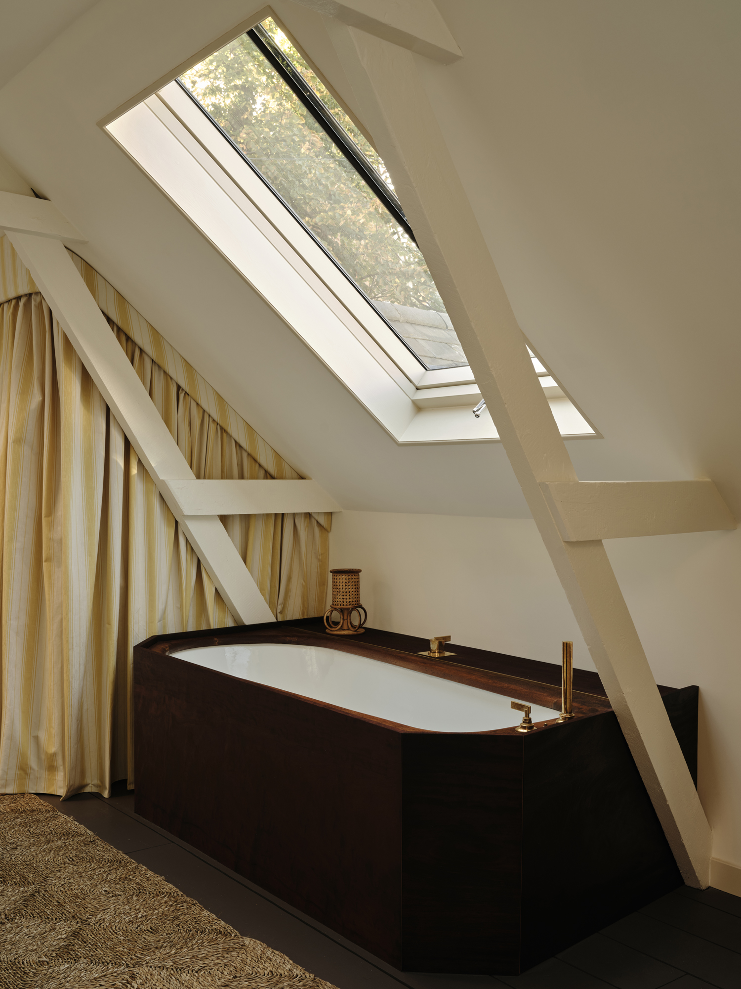 Attic bathroom with a dark wood bathtub, brass fixtures, and a skylight.