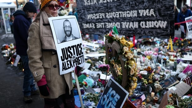 A woman stands at a makeshift memorial holding a sign